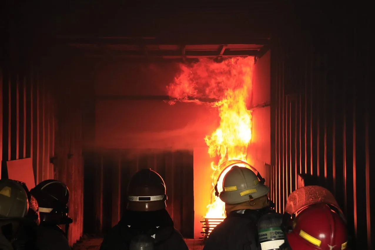 Ottawa Fire Services firefighters observing flame development during a live fire training evolution at the OFS Barnsdale Road facility
